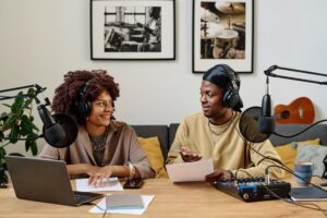 Two individuals wearing headphones collaborate on a laptop, focused on their work in a modern workspace.