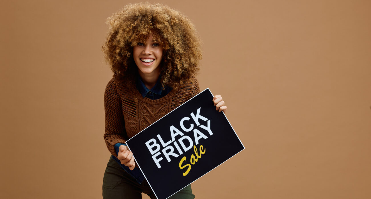 Young happy woman with Black Friday sale advertising banner against neutral background looking at camera. Copy space.