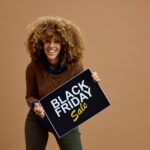 Young happy woman with Black Friday sale advertising banner against neutral background looking at camera. Copy space.