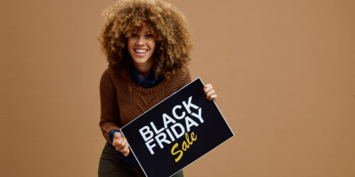 Young happy woman with Black Friday sale advertising banner against neutral background looking at camera. Copy space.